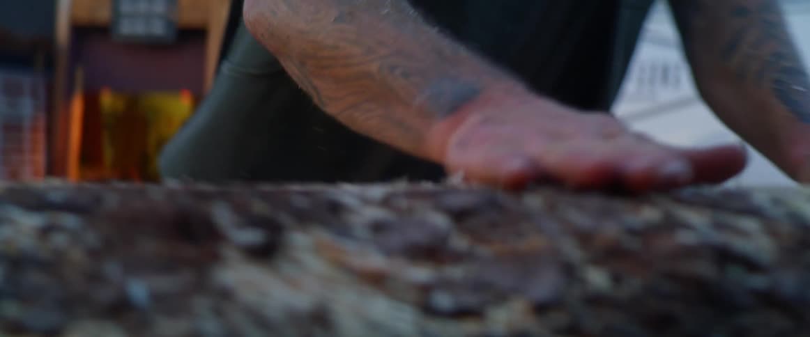 Man brushes sawdust off planed wood with commercial van in background