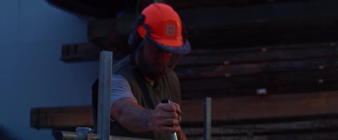 Man wears helmet and face shield while cutting log with machine
