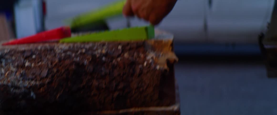 Man holding ax moves colorful wedge onto top of flat sawed log near parked work van