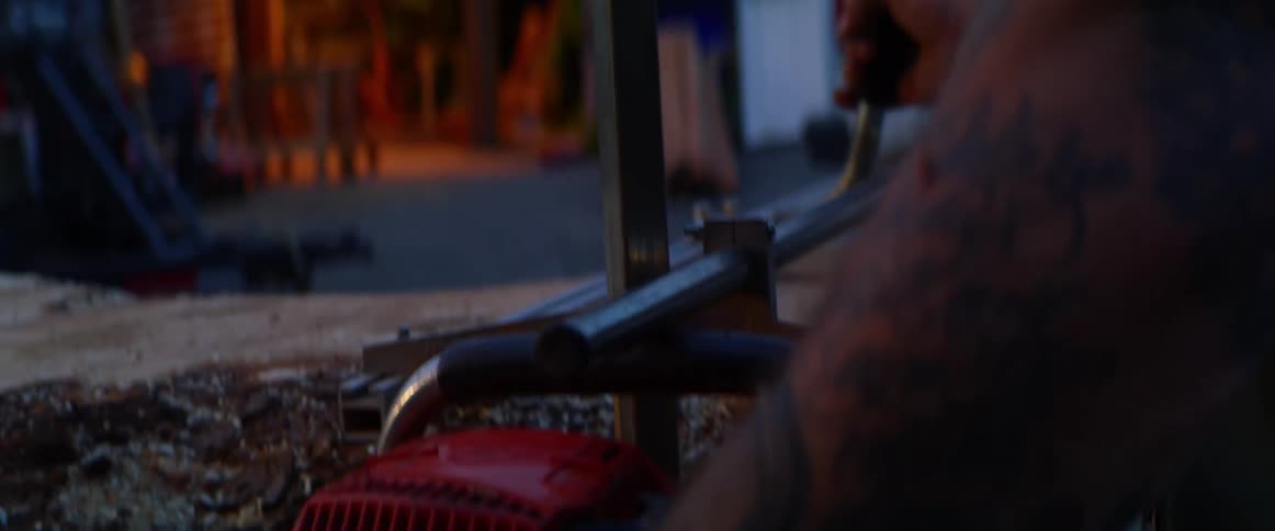 A man wearing a helmet and safety shield uses both hands on a power saw to slice a section of wood