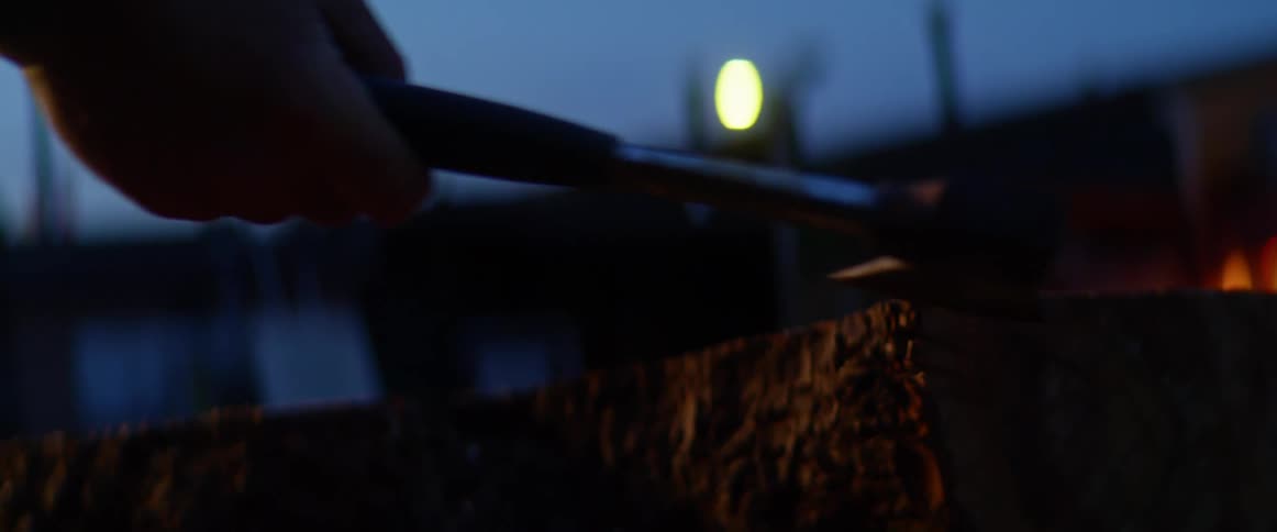 A man retrieves a hatchet driven into a log outside of a building at night