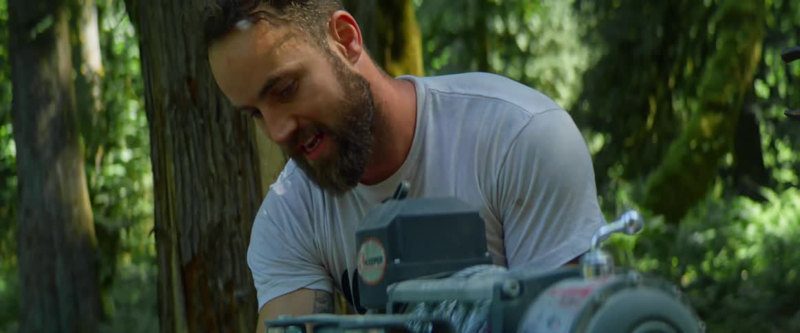 A bearded white male moves something from a white company truck to fix something outside near trees