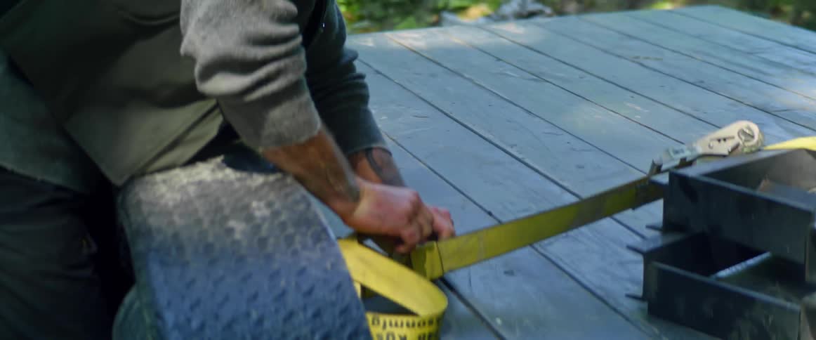 A man tightens a ratchet strap on the bed of a flatbed truck