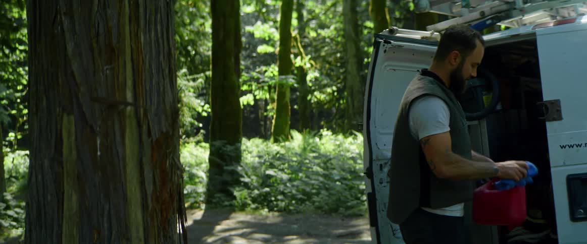 A man with a vest pouring gasoline into a chainsaw in a forest