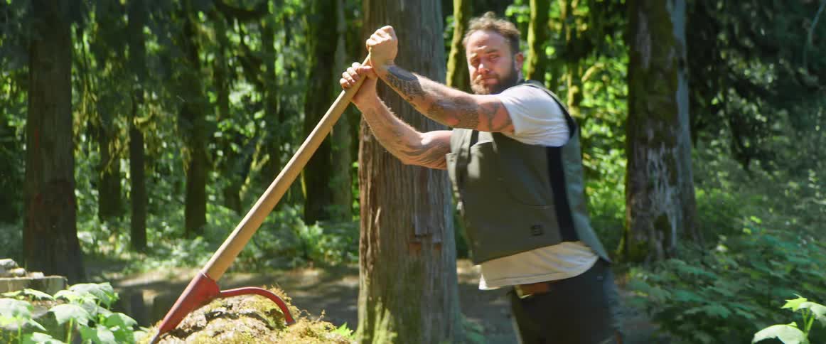 A man is moving a tree trunk in the woods