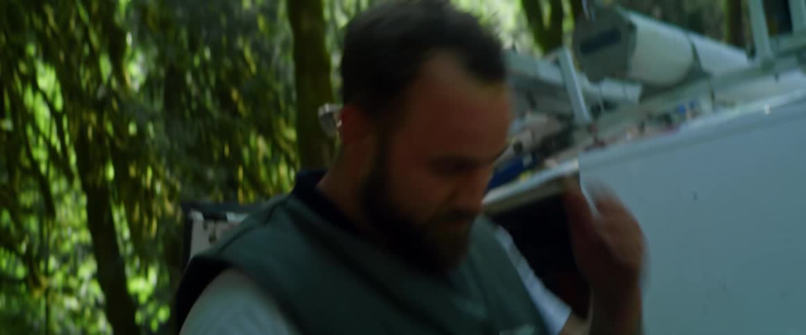 Man stands by open company van parked near woods wiping sweat off his face