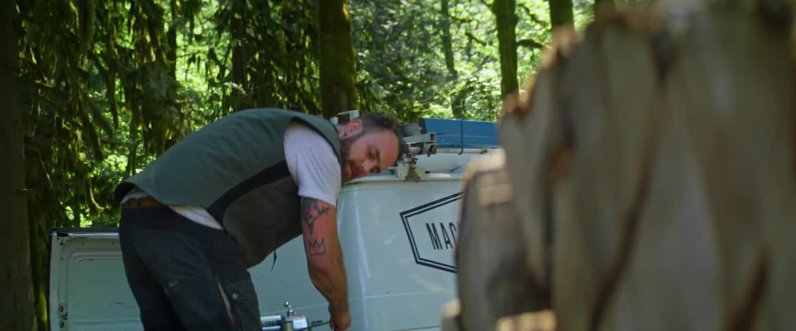 Man standing near commercial van parked near woods tugs on a cable to transport stacked logs