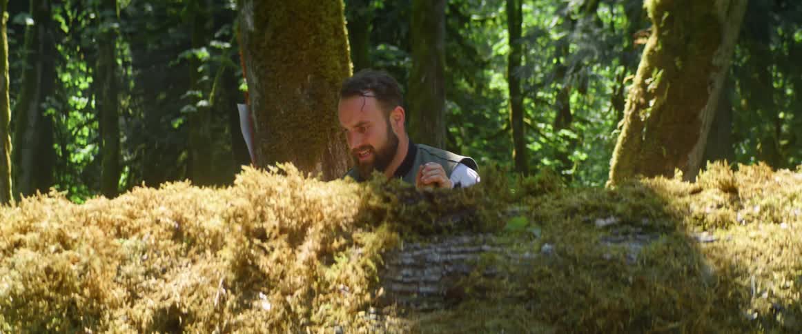 Man in forest works to move tree trunk with ax and strap