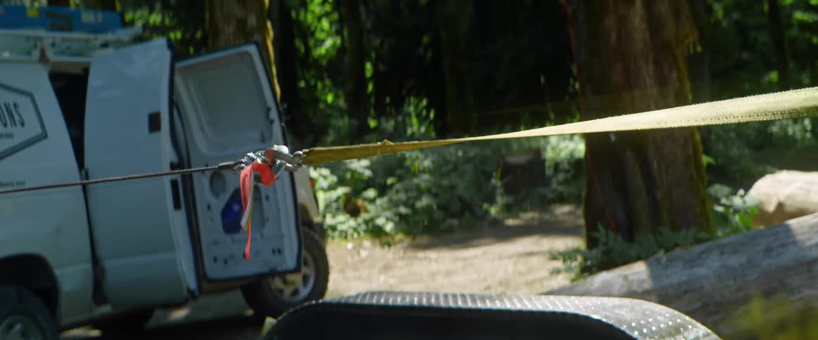 A log with moss on it being towed by a vehicle in the forest