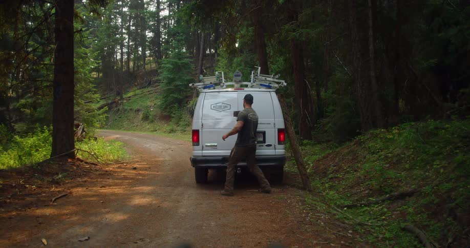 A man opens the back of his company van on a rural dirt road