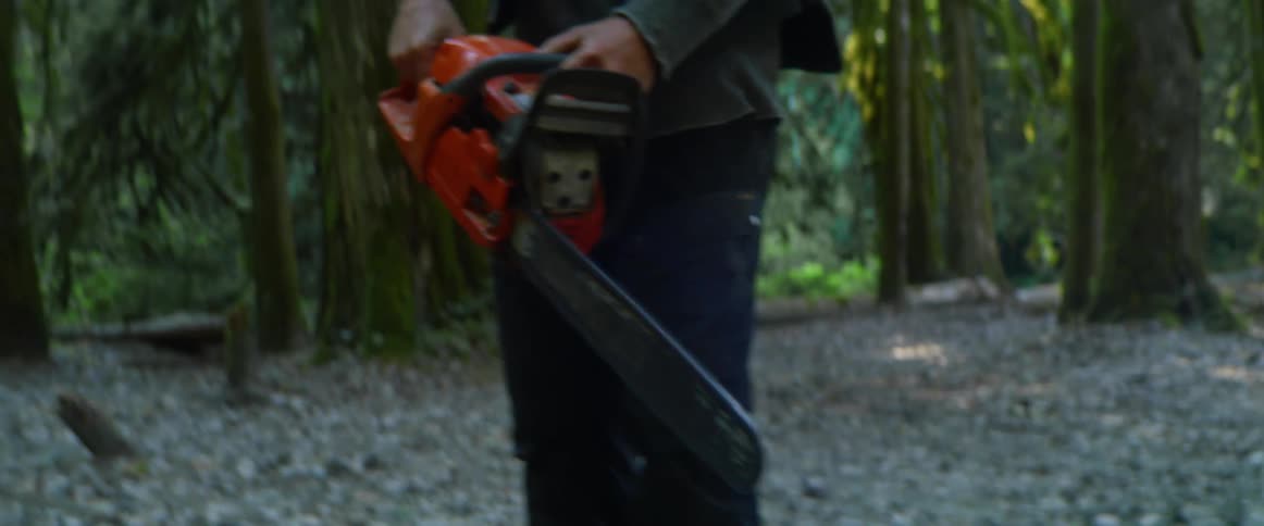 A man is holding a chainsaw in the forest