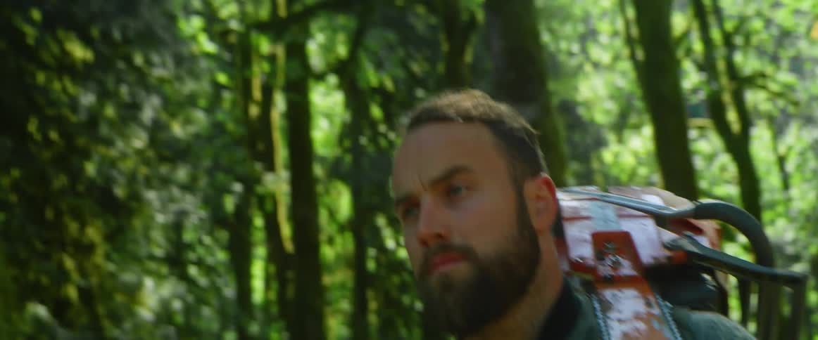 Man with a beard and a saw walks in the woods