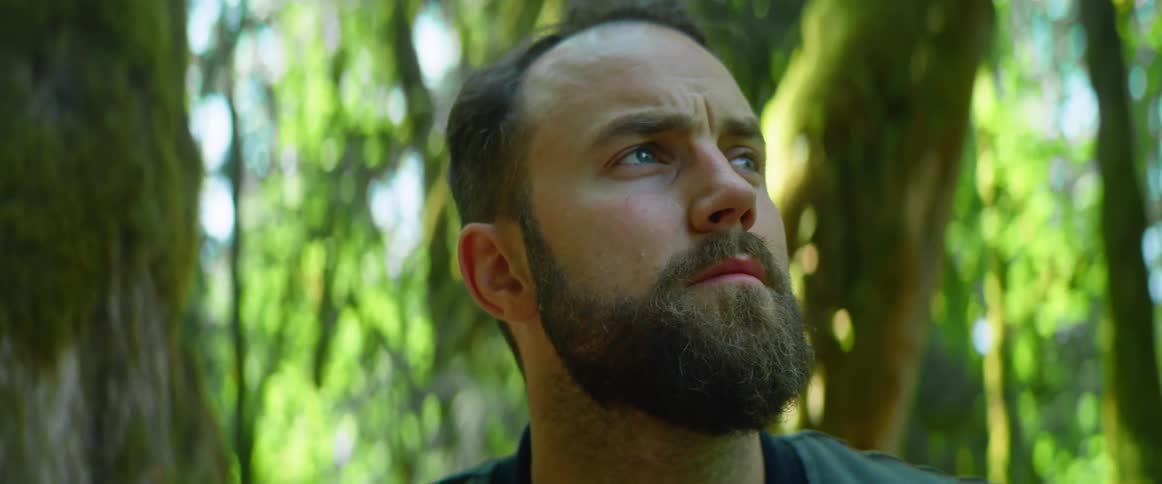 Man in woods looks around pensively