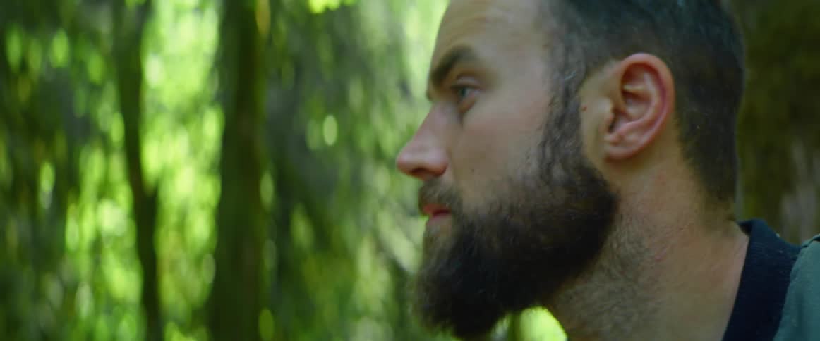 A man in a forest with trees leaves and sunlight in the background