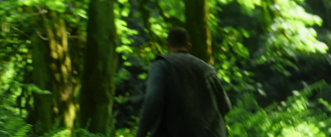 Man walks through forest carrying chainsaw