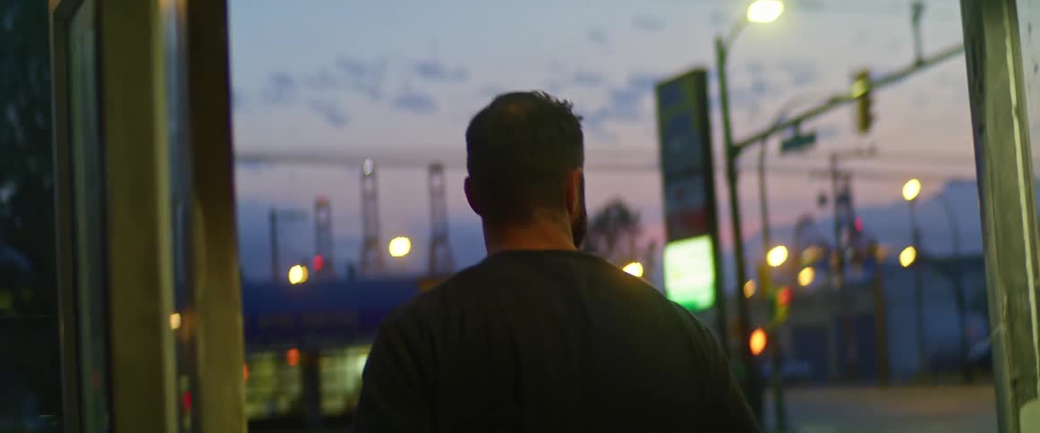 Man with a beard and sweatshirt leaves the store through the front door at dusk