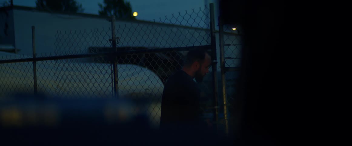A man unlocks and opens a large chain link gate in the early morning