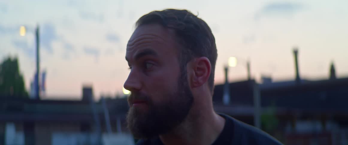 A man standing and staring with buildings the sky and clouds in the background