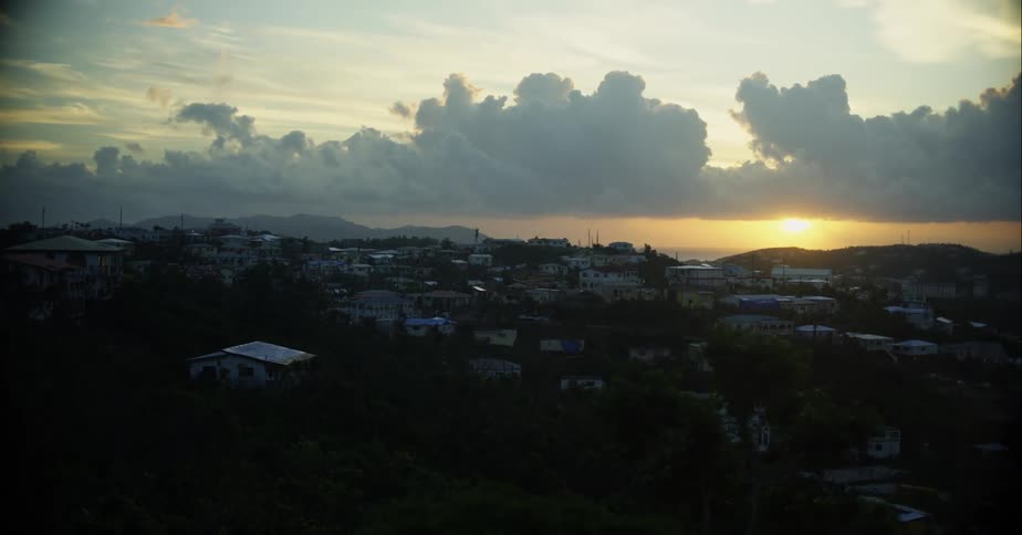 Thick clouds loom over a small town in the hills at sunset