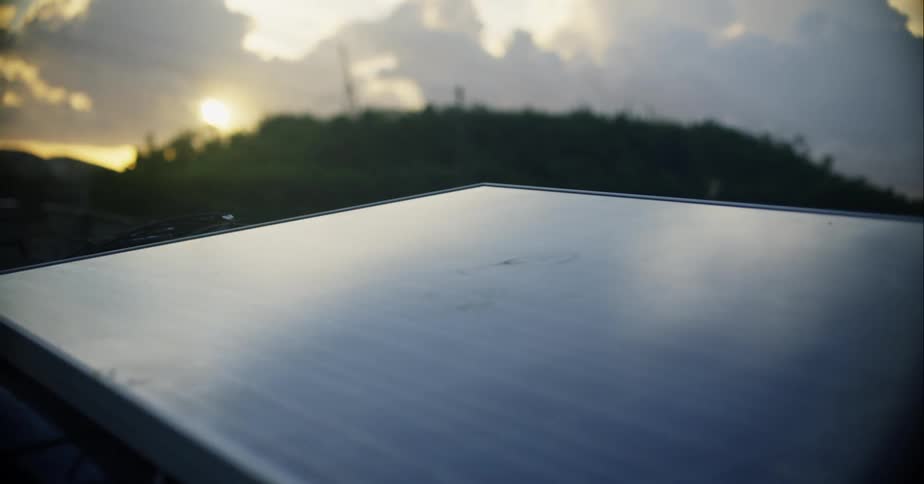 A solar panel with wires with a hill the sun the sky and clouds in the background