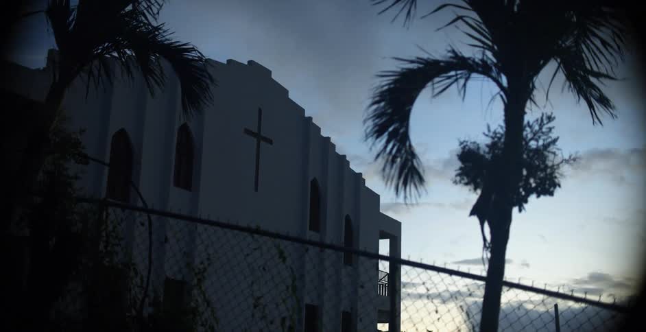 Mission style church building behind fence and palm trees at dusk