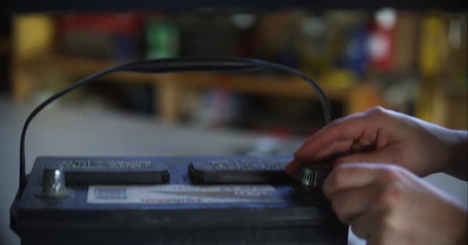 Person connects wire to battery sitting on work table