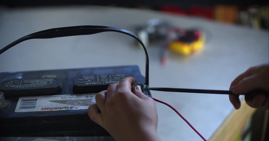 A man uses a long screwdriver to tighten a car battery