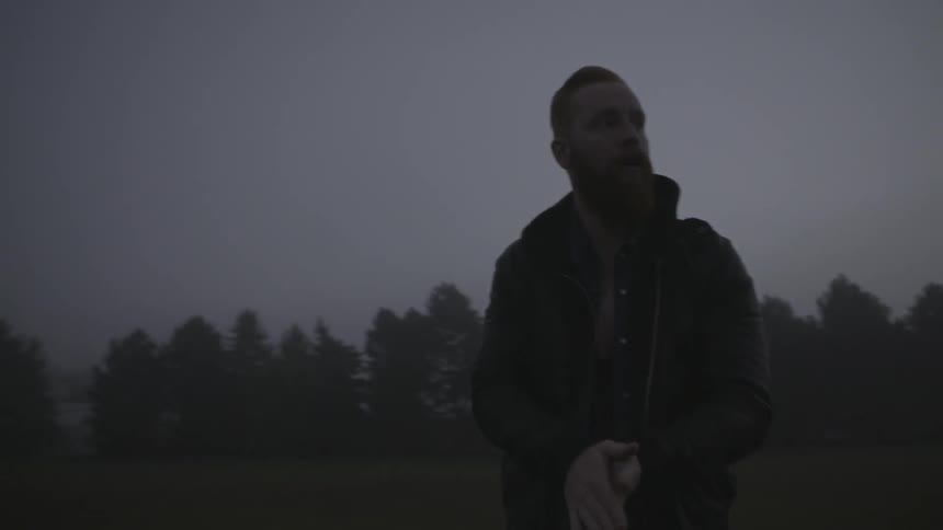 A man stands outside rubbing his hands together and blowing on them to keep warm