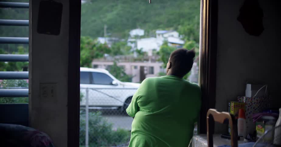 A woman stands in the open doorway of her apartment and looks outside
