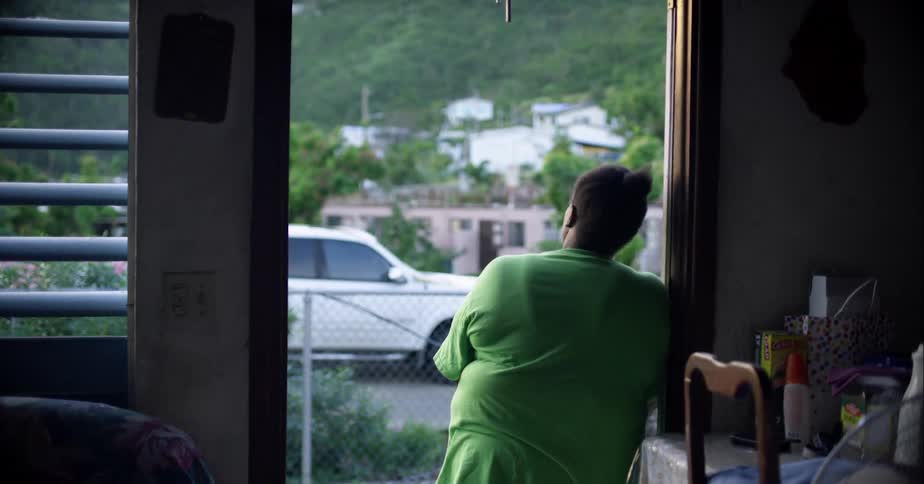 A woman leans against the frame of her front door as she gazes outdoors