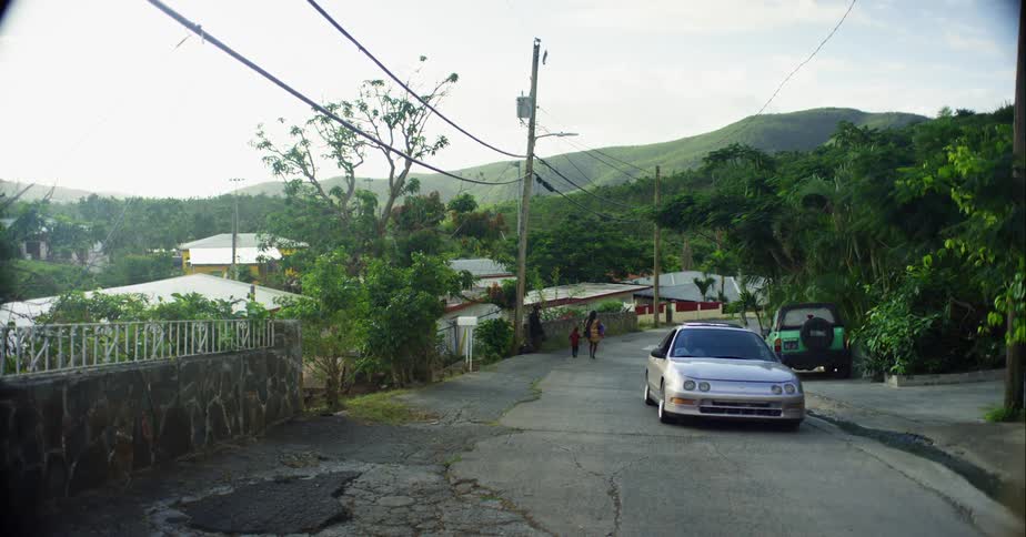 Two people walk on the side of the road in a neighborhood when a car passes them