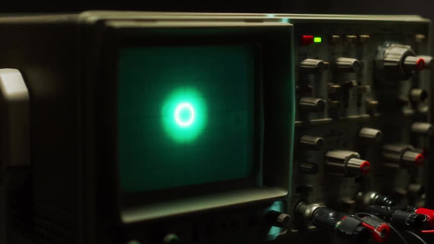 A green light flashes on an oscilloscope screen next to knobs and dials