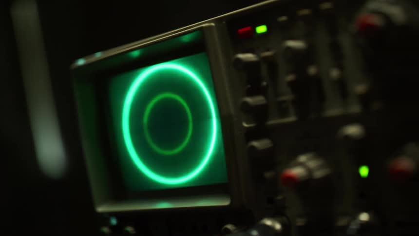 A small monitor shows a green circle changing in thickness as a laser flashes across the screen and onto the oscilloscope the screen is attached to