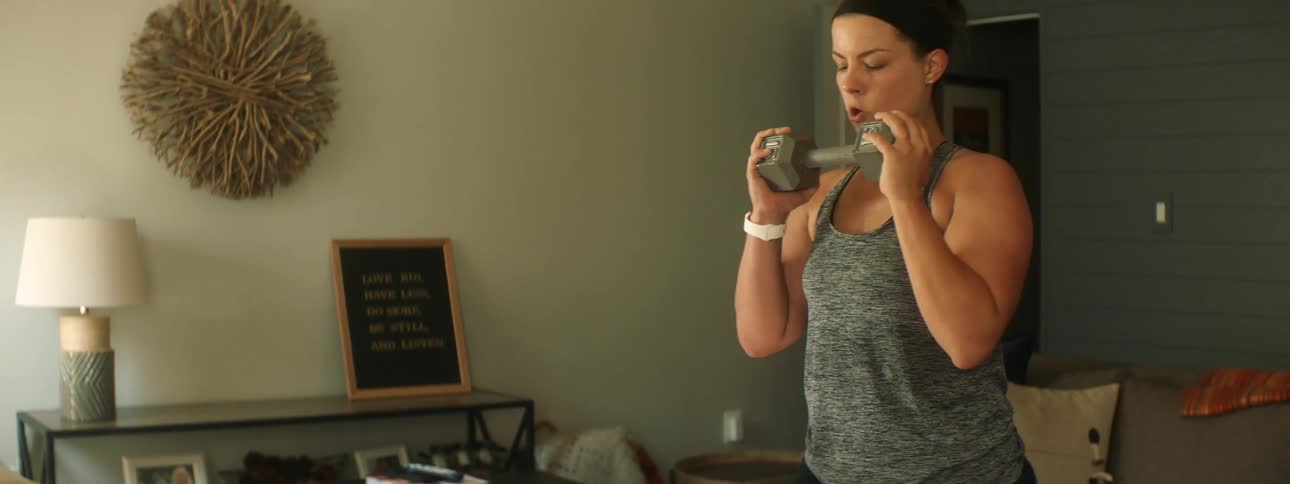 Woman with a grey sport top works out with a dumbbell