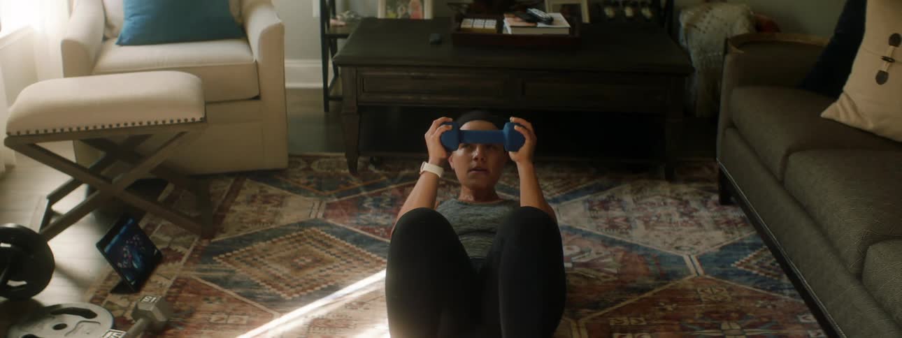 A woman at home exercises to a video she is watching on a tablet