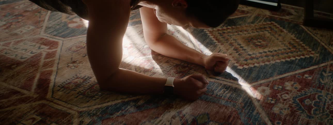 A woman at home exercises along with a video she watches on a tablet