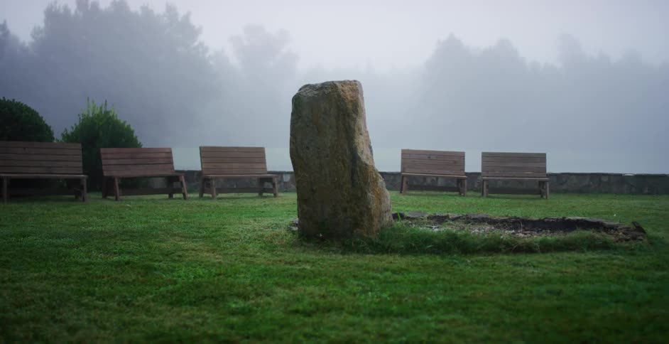 Benches in a park sit in a semi circle facing a large rock display near a forest