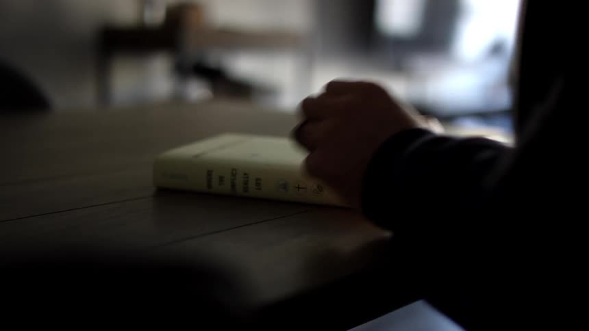 Man with a black sweater sits at table and turns the pages of a book