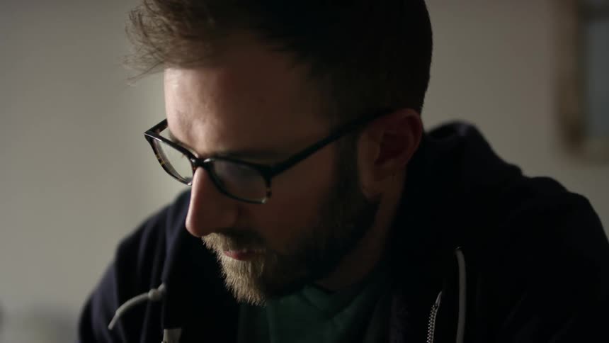 A man is sitting in a room and wearing glasses