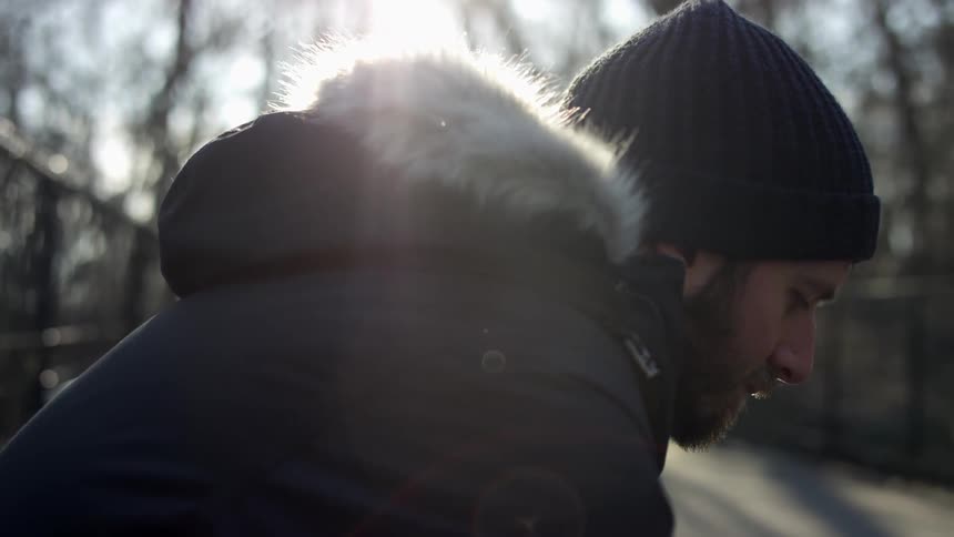 A man sitting outside with his head hung down low throws a stick for two dogs