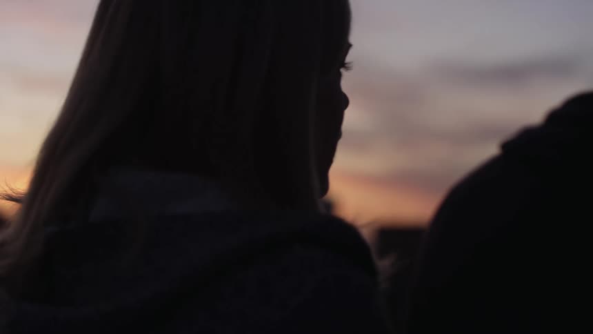A teenage girl and boy sit outside and talk