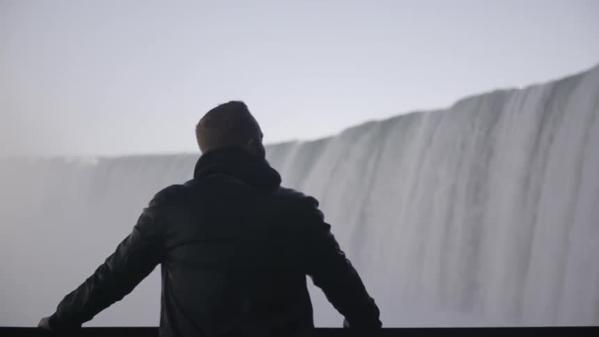 A man is facing a waterfall and viewing it