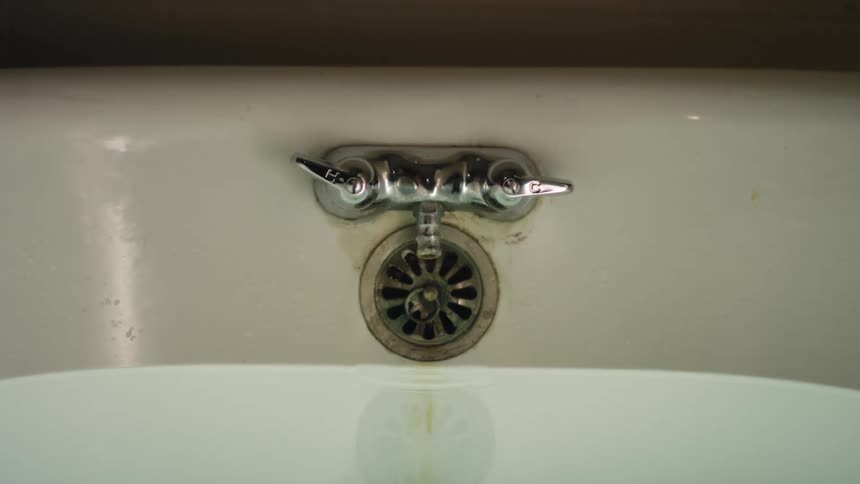 Drops of water fall from a faucet into a bathtub filled with water