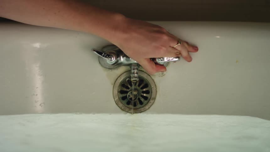 Woman turns off water then runs hand through bath water
