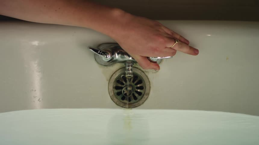 A person turning on a bathtub faucet