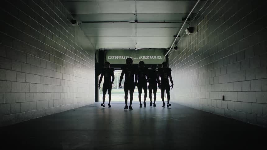 A group of football players walk down a dark hall from a field