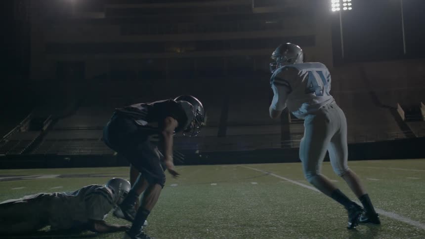 A football player is tackled on a field at night