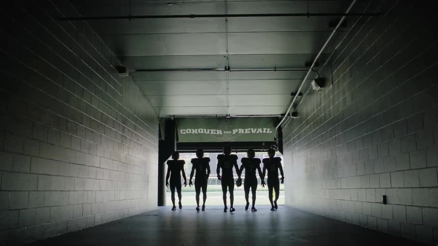 Members of a football team walk down a dark hallway