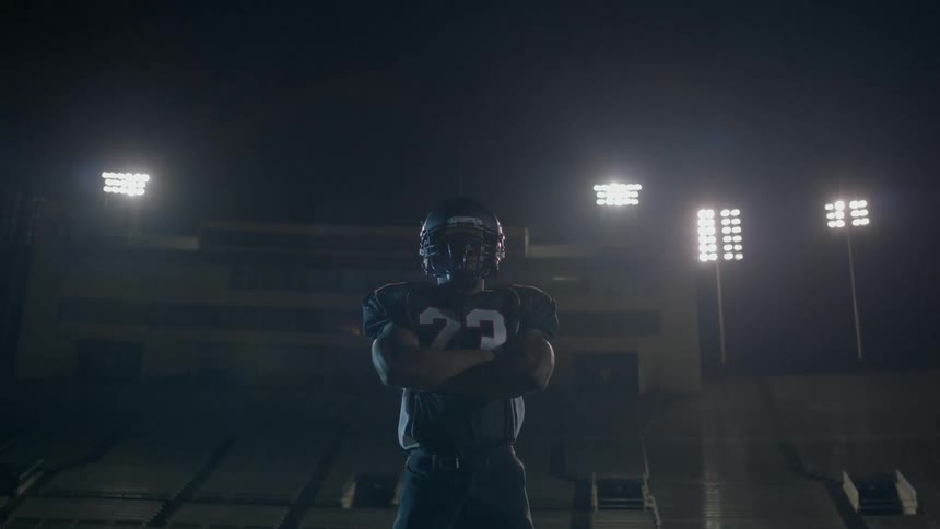 A football player stands alone on a football field at night