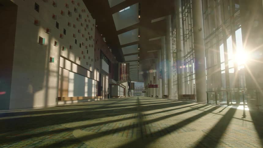 A long hall has walls made of glass on the side with the sun coming in